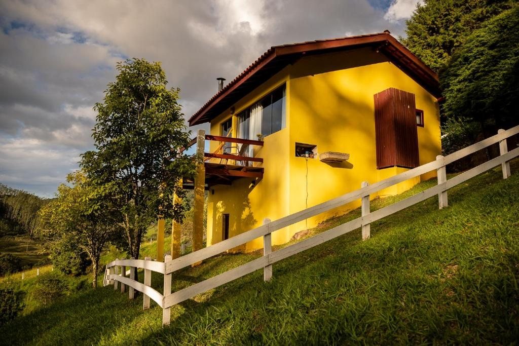 Chalé amarelo com varanda no gramado, entre árvores e montanhas